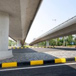 Vias elevadas de concreto sobre uma rodovia, cercadas por áreas verdes em um trecho urbano.