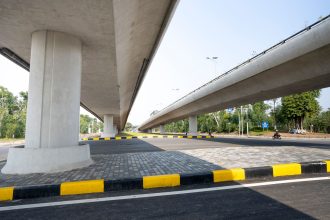 Vias elevadas de concreto sobre uma rodovia, cercadas por áreas verdes em um trecho urbano.