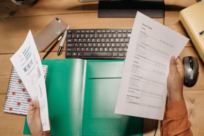Mãos analisam planilhas financeiras sobre uma mesa, ao lado de um teclado e materiais de escritório.