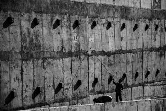 Dois trabalhadores pintam uma grande parede de concreto durante um serviço de manutenção em Londrina, no Paraná.