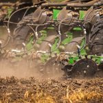 Máquina agrícola semeia um campo de solo seco durante o plantio.